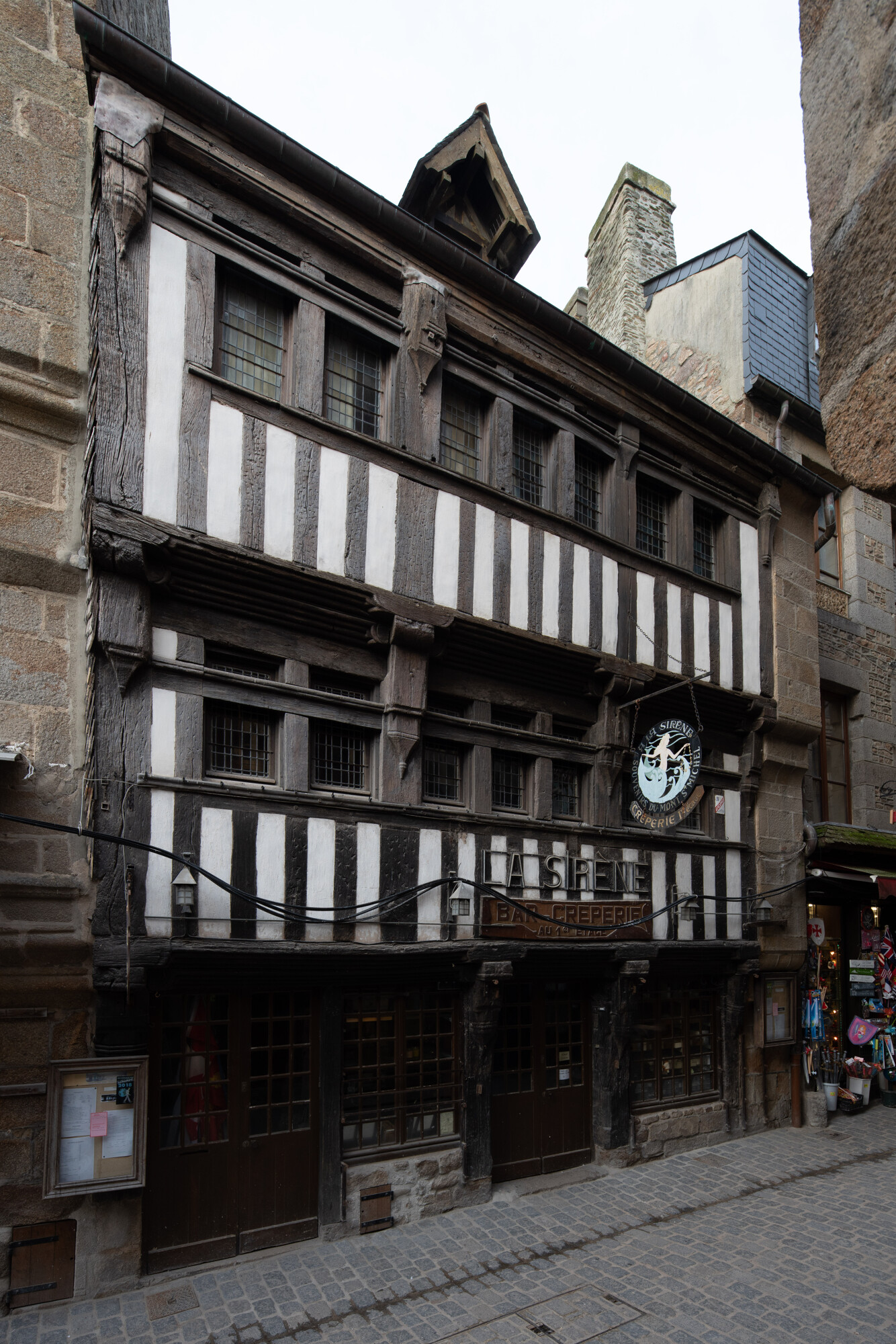 La façade sur rue de la maison La Sirène se compose d’une structure en pan de bois (chêne) entre deux murs maçonnés. L’ossature principale s’organise en trois travées de poteaux porteurs courts qui permettent une élévation en surplomb des deux étages. Elle est datée par analyse dendrochronologique entre 1462d et 1482d. © Région Normandie – Inventaire général, Patrick Merret